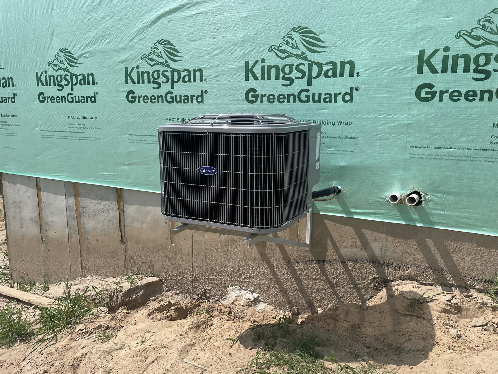 A wall-mounted condenser on a wrapped new build
